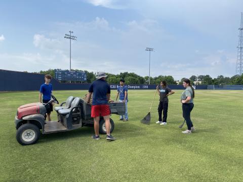 students working on baseball field with side by side vehicle. 